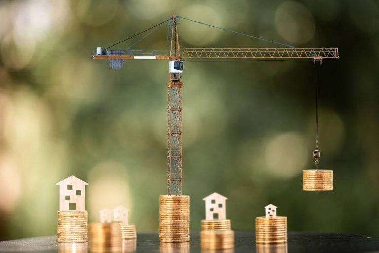 model construction crane and wooden home cutouts on top of stacks of coins
