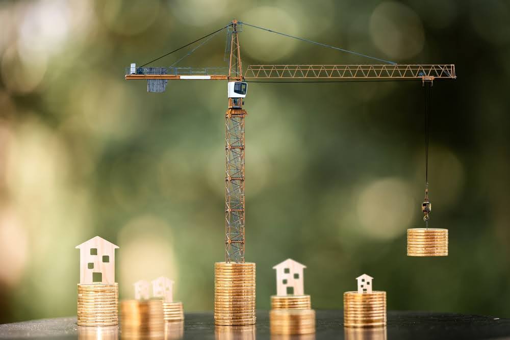 model construction crane and wooden home cutouts on top of stacks of coins
