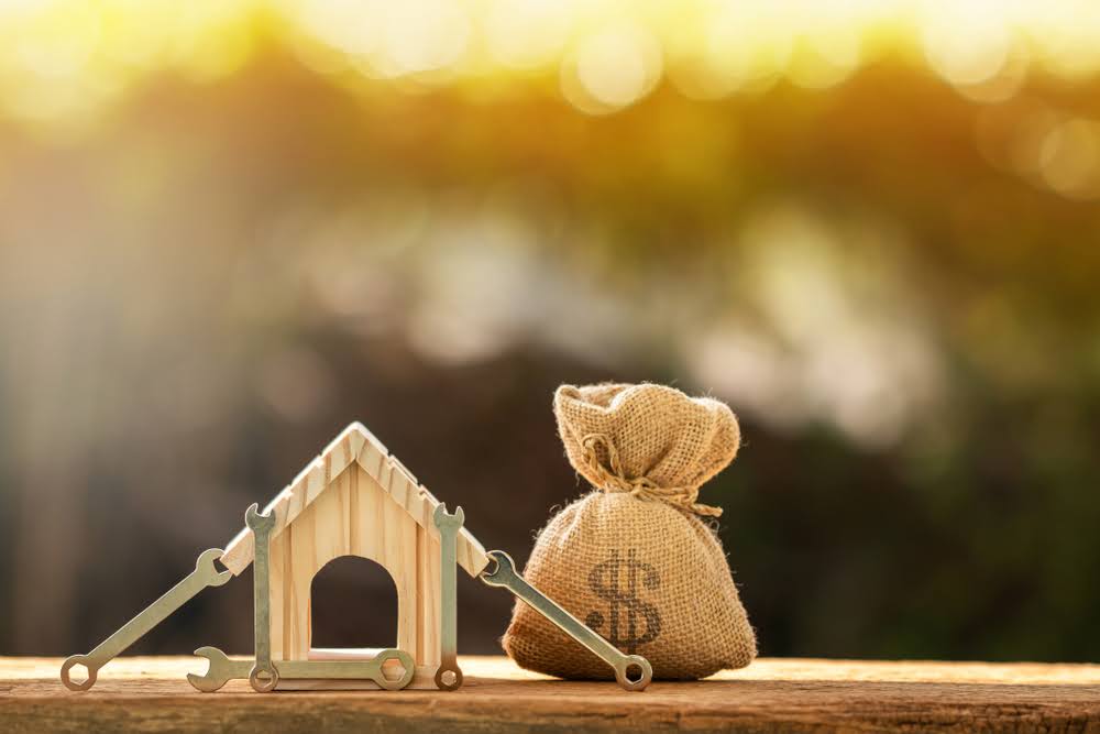 small home facade made out of wood next to a small model sack of money